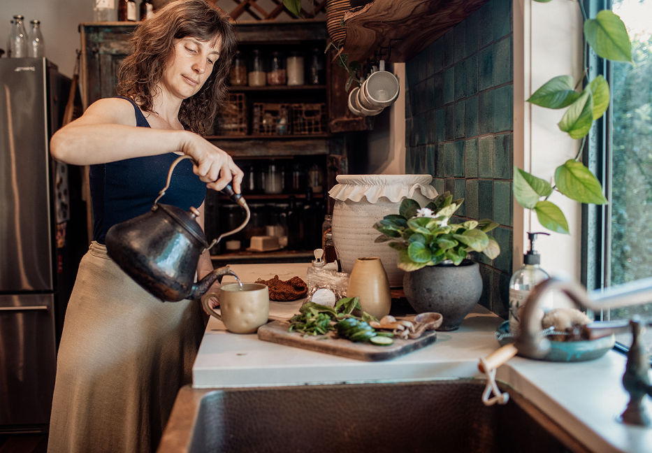 Cat Green - pouring tea from kettle with chopping board of veggies in on bench. making herbal remedies - how to study herbs and use natural remedies at home. DIY Immunity Remedy Kit and Immunity online course | Everyday Empowered