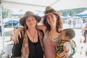 Gorgeous friends smiling at Sunny Coast HerbFest, herbal medicine event on the Sunshine Coast. Image of two women smiling, with one holding a baby.