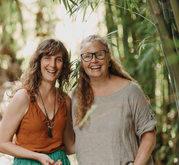 Image of Cat Green and Heidi Merika, smiling, standing in front of bamboo. Herbal educators and community herbal medicine events. Everyday Empowered