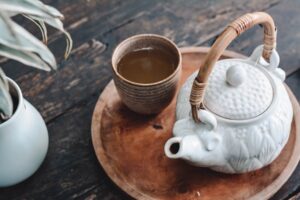 Image of ceramic mug of herbal tea next to white teapot with natural handle, on a wooden plate. Herbal Tastes