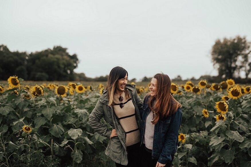 Image of 2 women laughing in a field of sunflowers. For Nonviolent Communication foundation training on the Sunshine Coast.