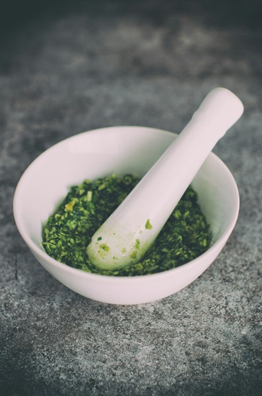 foraged wild weed pesto - kitchen medicine and wild medicinal plant herbal remedies to use everyday. picture is of white mortar and pestle with green pesto in it.