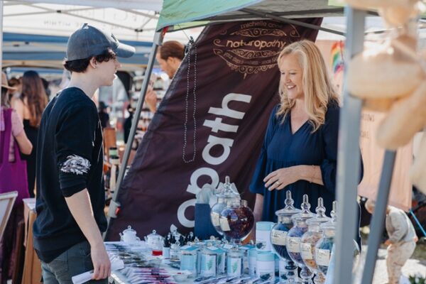 Image of man talking to smiling woman at herbal medicine stall at herbal medicine community gathering HerbFest on the Sunshine Coast in Coolum