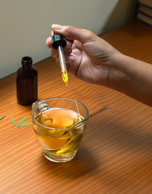 Image of someone adding herbal bitters tincture to glass of tea because bitters support digestion