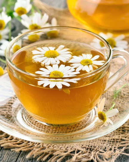 Build your back-to-school herbal toolkit. Image is of cup of chamomile tea in a glass teacup with 3 chamomile flowers floating on the top. 