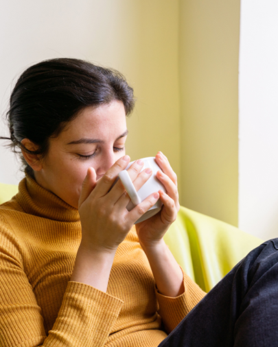 woman holding white mug up to her face, drinking tea, reflecting on herbal tastes