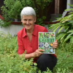 Image of Pat Collins smiling holding one of her wild medicinal weeds books.