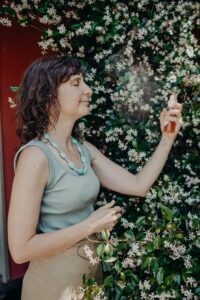Image of Cat Green standing in front of flowering jasmine, spraying her face with after-sun spray as a summer herbal remedy for sunburn